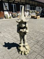 Gartenzwerg aus Beton mit Hut stehend auf Baumstumpf