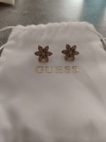 Goldene GUESS-Ohrringe in Blumenform mit Strasssteinen.