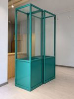 2 hohe Glasvitrinen mit türkisfarbenem Metallrahmen