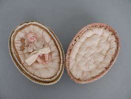 ANTIKES BÉBÉ-EI MIT ZELLULOIDPUPPE, KARTONAGE, STICKEREI