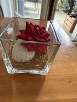 Glasvase mit roter Kunstblume und Steindekoration