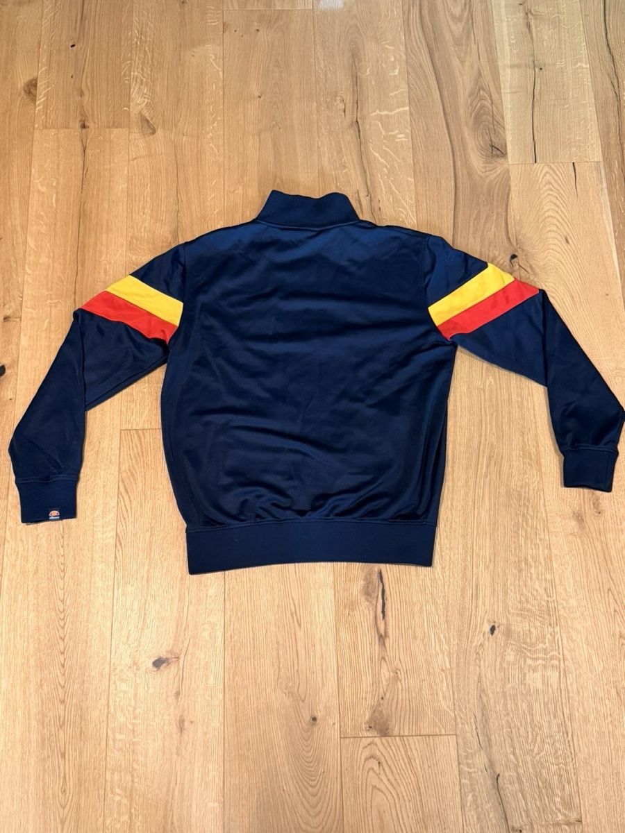 Ellesse Giacche: Ellesse navy blue track jacket with yellow and red diagonal  – Usato da Pfaffhausen venduto da placard 1