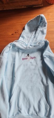 Light blue hoodie with "Never Again" print, size S