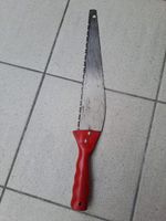 Gebrauchte Baumsäge mit rotem Griff für Gartenarbeit.