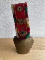 Kuhglocke mit rotem Lederriemen und bunten Fransen