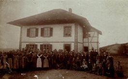 Kindergruppe mit Erwachsenen vor Riegelhaus (Schulhaus)