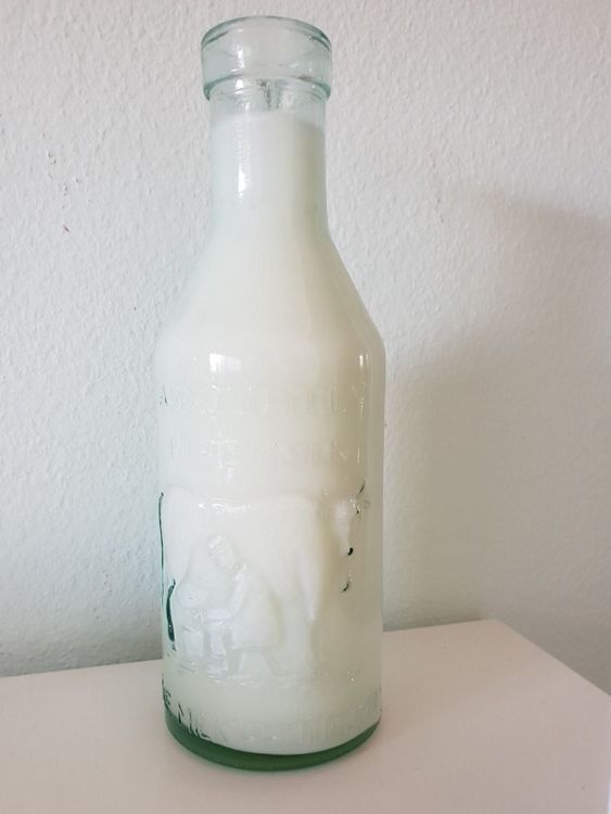 Produktbild von Süße Kuh Sitzen Und Halten Milchflasche Tier Maskottchen Cartoon Vektor Illustration Stock