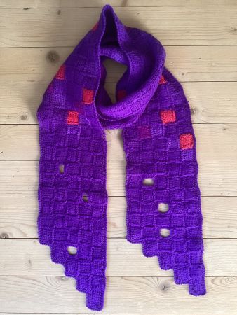 Handgestrickter, violetter Schal mit Farbtupfern.