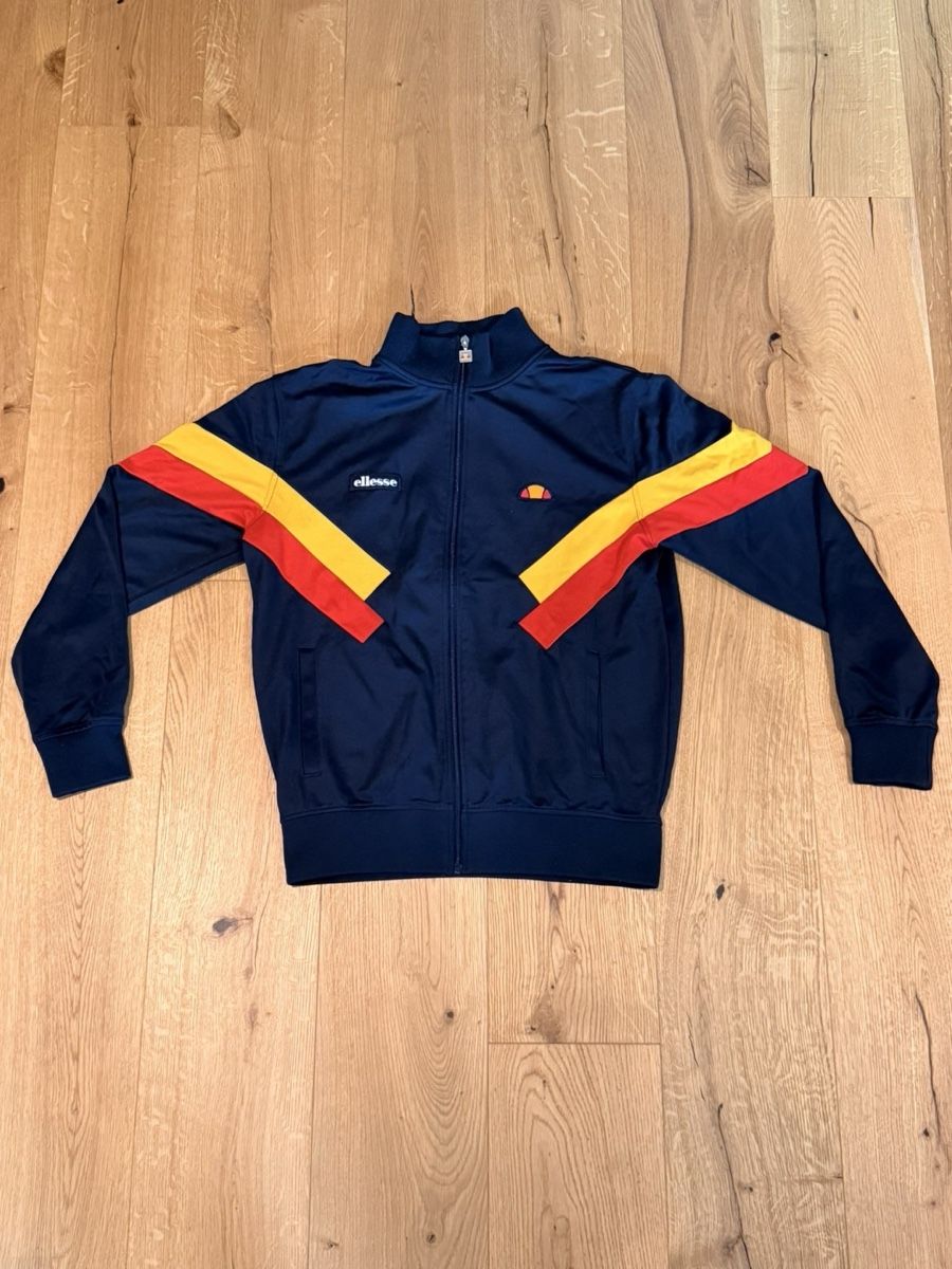 Ellesse Giacche: Ellesse navy blue track jacket with yellow and red diagonal  – Usato da Pfaffhausen venduto da placard