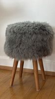 Hocker aus Schafsfell in grau mit Holzbeinen