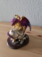 Sammlerstück: Funkelnder Drache auf rissigem Ei mit Münzen