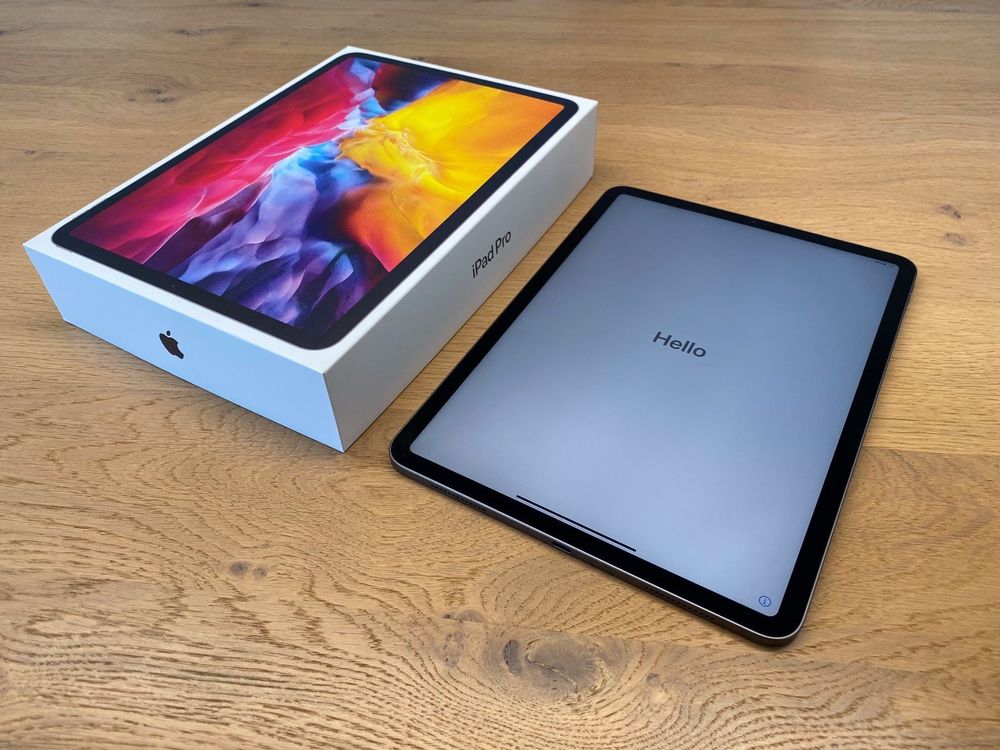 On a wooden table is an open white box labeled iPad Pro, and next to it is an iPad Pro displaying the Hello screen.